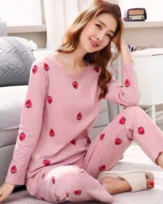 Pink long sleeve pajamas with strawberry pattern for women worn by a woman in a house