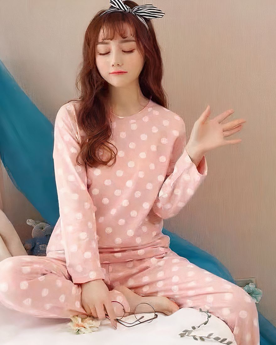 Long sleeve pink pajamas with white dots pattern for women worn by a woman wearing a bandana in a house
