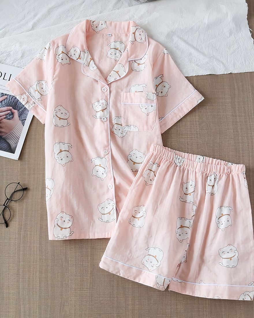 Light pink short sleeve pajamas with cat print for women on a table with a bezel and a book on the side