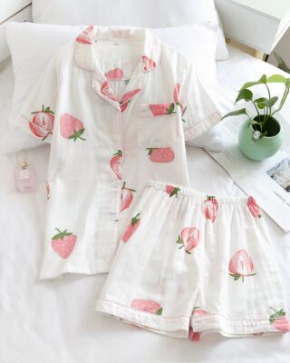 Short sleeve summer pajamas with strawberry print for women on a bed with a small vase and a flower inside a house