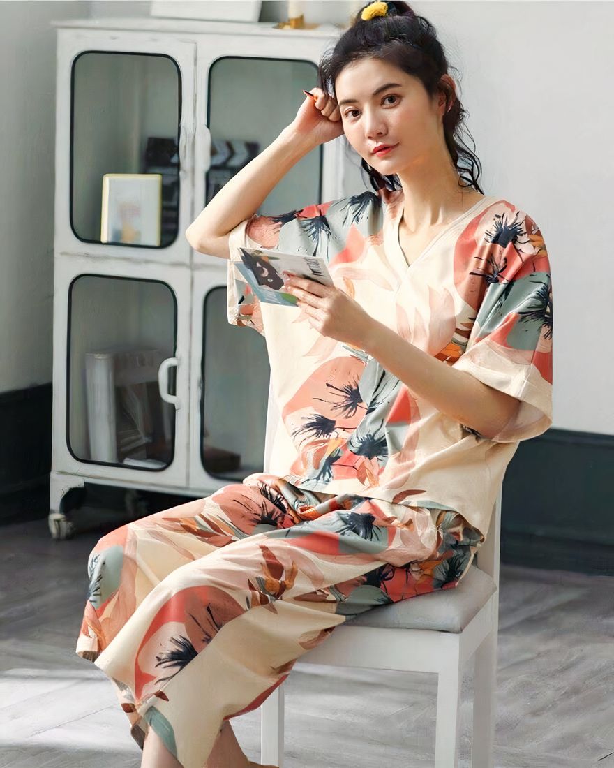 Two-piece summer pajamas with V-neck and floral pattern worn by a woman sitting on a chair in a house