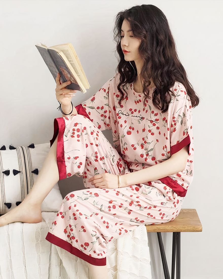 Women's bat sleeve pajamas with red flower print worn by a woman reading a book sitting on a chair in a house