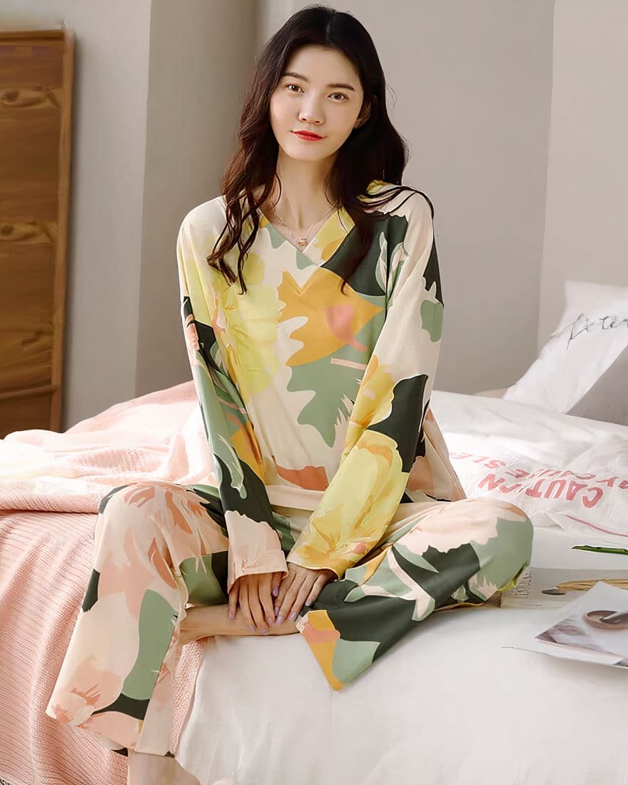 Women's long-sleeved pajamas with V-neck and floral pattern worn by a woman sitting on a bed in a house