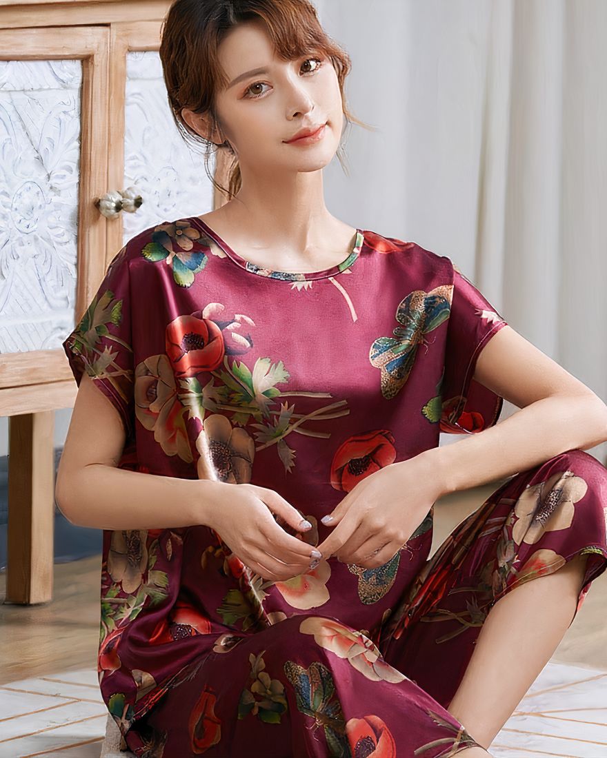 Red silk satin summer pajamas with flower print for women worn by a woman sitting on a carpet in a house