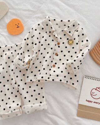 White pajamas with black polka dots and a yellow smiley logo on a white sheet with small toys around