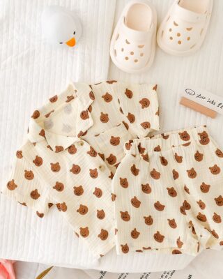 Off-white child's pajamas with bear design on a white table with a small white duck toy and pink fangs