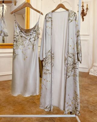 Sexy grey pyjamas with floral print hanging on a hanger in a room with wooden floor and white wall and in front of a large mirror with golden frame