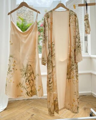 Sexy beige pyjamas with floral print hanging on hangers in a room with wooden floor and white wall and in front of an open window