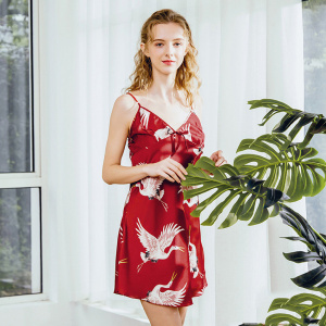 Red babydoll pajamas with stork motifs worn by a woman standing in front of a plant and a white wall