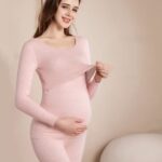 Pink pregnancy pajamas, worn by a woman holding her stomach in front of a beige wall