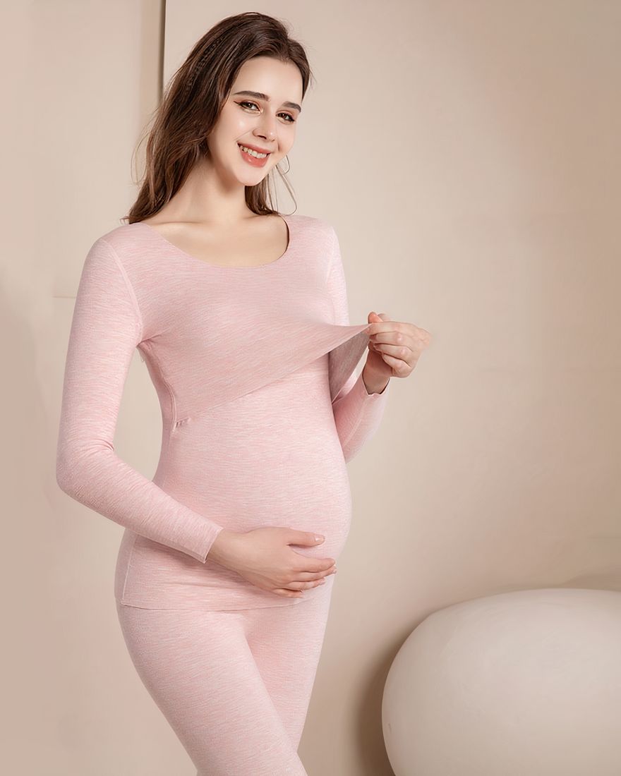 Pink pregnancy pajamas, worn by a woman holding her stomach in front of a beige wall