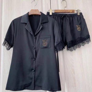 Women's black pyjashort with gold logo and lace, hanging on a hanger in front of a beige wall