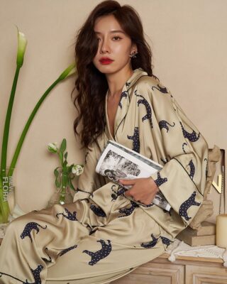 Beige pyjamas with leopard print worn by a woman sitting on a piece of furniture holding a magazine in front of a beige wall