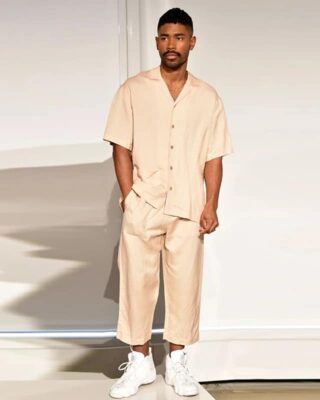 man standing in front of a white wall, wears light beige summer pajamas for men, consisting of pants and a short-sleeved shirt