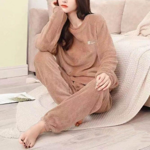 young woman wears a pyjama in beige pilou pilou, she is sitting on a plaid near a sofa, on the floor, the chin leaned in one of her hands