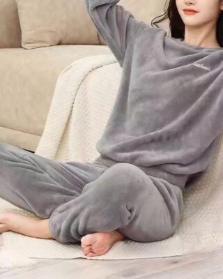 young woman wears a pyjama in grey pilou pilou, she is sitting on a plaid near a sofa, on the floor, hands crossed behind her head