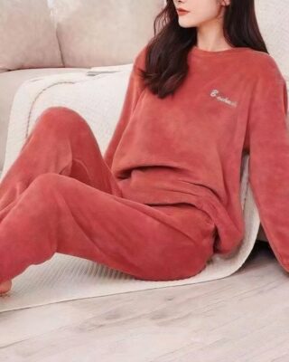 young woman wears a pyjama in red pilou pilou, she is sitting on a plaid near a sofa, on the floor